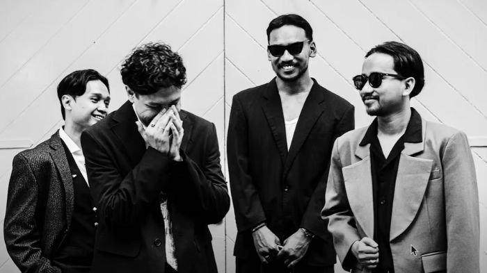 Four members of a band pose playfully in a black and white setting, showcasing their unique fashion and camaraderie.